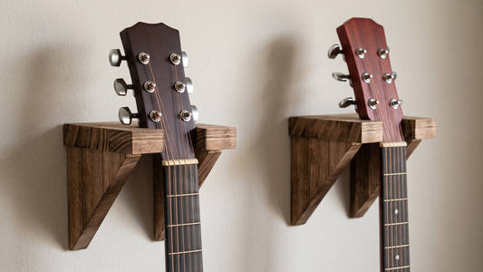 Two triangular solid wood wall hangers holding acoustic guitars by the headstock